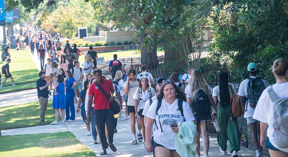 A large group of students walks along a sidewalk to classes.